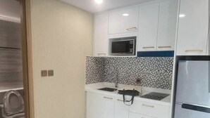 A modern kitchen with white cabinets, a black and white tiled backsplash, a microwave, a stove, and a refrigerator. - Stunning 1 bed apartment in Lamung District (Thailand)