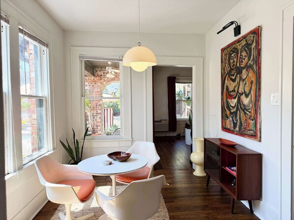 A modern living room with a round table, two chairs, a pendant light, a bookshelf, and a large abstract painting.