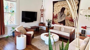 Una sala de estar moderna con un televisor de pantalla plana, un gran tapiz y una lámpara colgante de macramé.