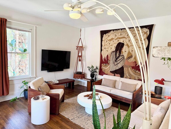 Una sala de estar moderna con un televisor de pantalla plana, un gran tapiz y una lámpara colgante de macramé.