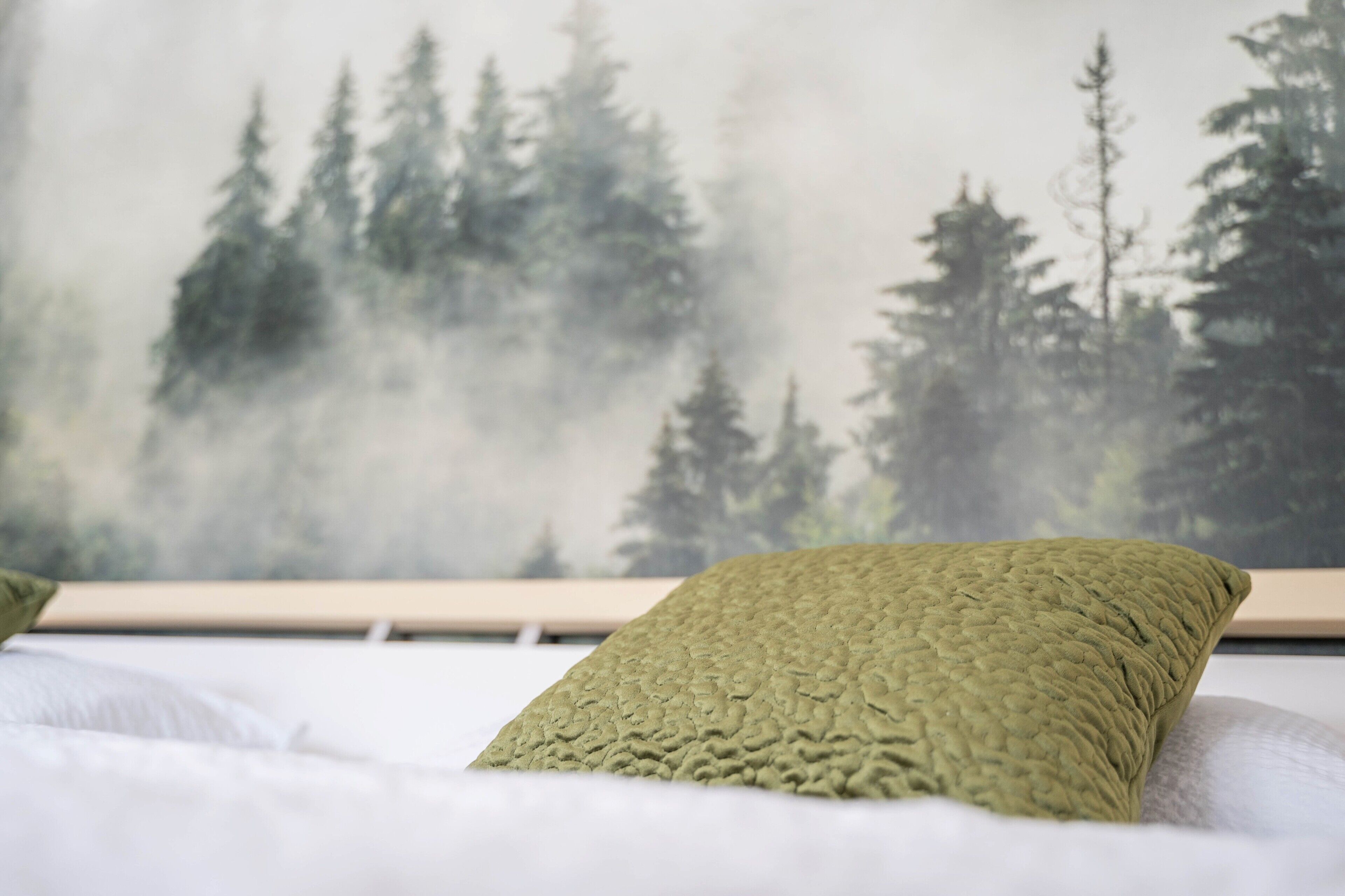 Una cama con un almohadón verde con textura y un mural temático de bosque.