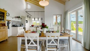 A modern kitchen with white cabinets, a wooden dining table, and a view through the glass door. - Holiday Home "Waldwasserhaus Leisel" with Mountain View, Private Terrace & Wi-Fi (Leisel)