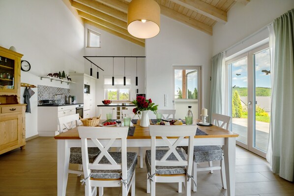 A modern kitchen with white cabinets, a wooden dining table, and a view through the glass door. - Holiday Home "Waldwasserhaus Leisel" with Mountain View, Private Terrace & Wi-Fi (Leisel)
