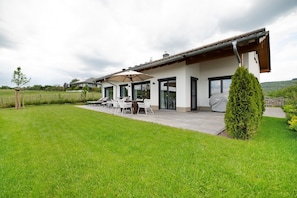 A modern house with a patio, outdoor seating, and a well-maintained lawn. - Holiday Home "Waldwasserhaus Leisel" with Mountain View, Private Terrace & Wi-Fi (Leisel)