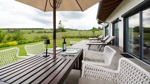 A covered patio with a table and chairs, a bottle of wine, and a view of the countryside. - Holiday Home "Waldwasserhaus Leisel" with Mountain View, Private Terrace & Wi-Fi (Leisel)