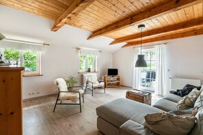 Un salon avec un plafond en bois, un canapé, un fauteuil, un téléviseur et une fenêtre.
