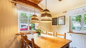 Een eetgedeelte met een houten tafel, stoelen, hangende rieten hanglampen en een raam met uitzicht op het exterieur.