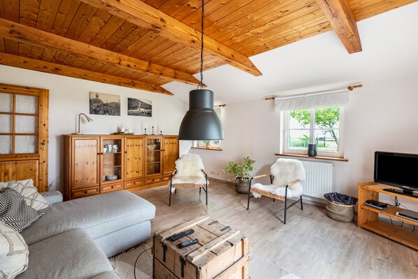 A cozy living room with wooden beams, a sofa, chairs, a television, and a cabinet.