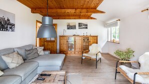 Een woonkamer met een bank, een salontafel, een hanglamp, een houten kast en een raam met een plant.
