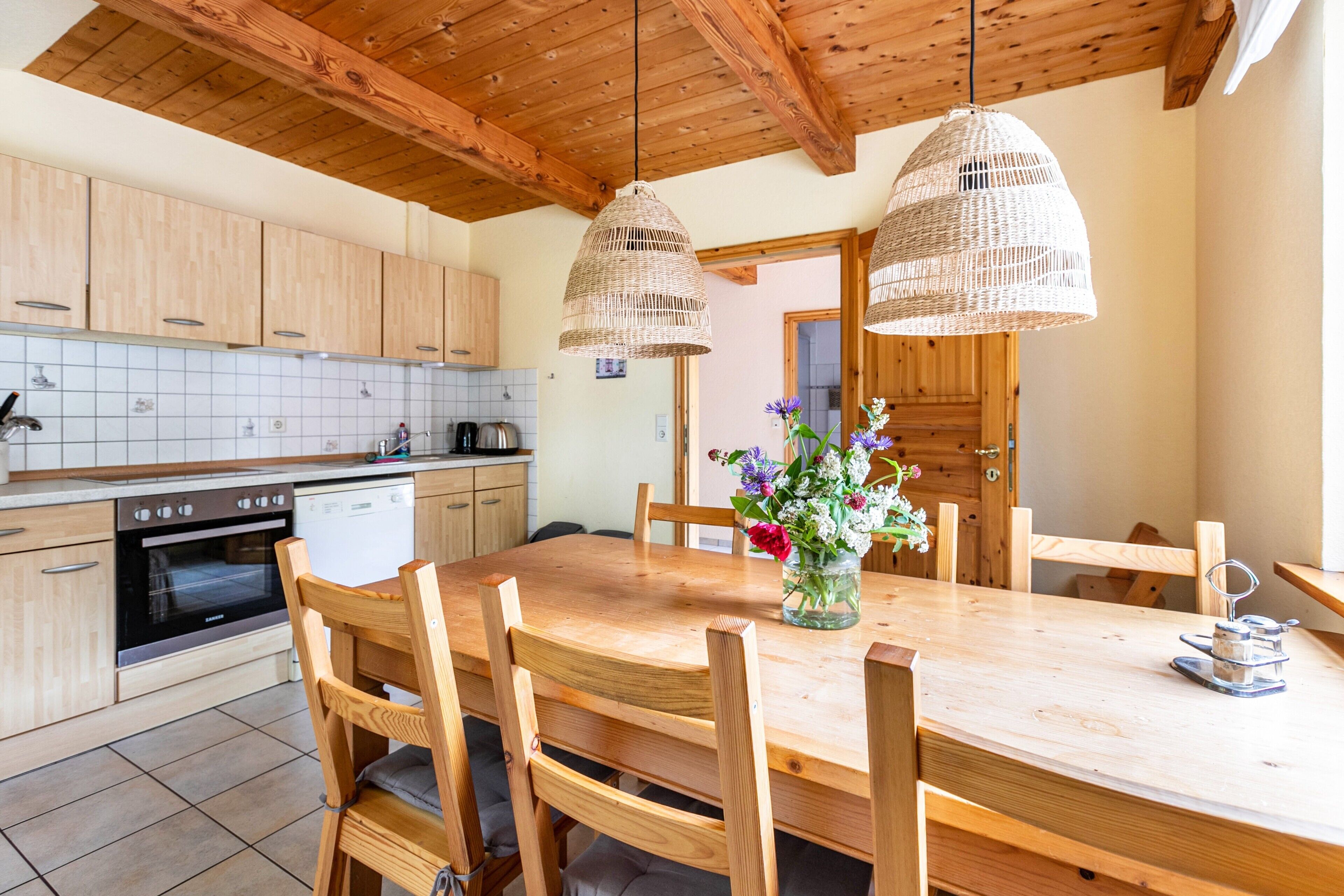 Una cucina con mobili in legno, un tavolo da pranzo, sedie e lampadari in vimini appesi.