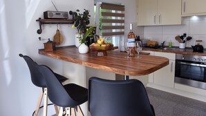 Una cocina con una mesa de madera, sillas negras, una radio, una planta, un frutero y una copa de vino.