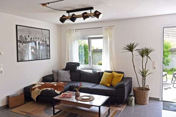 Un salon avec un canapé, une table basse, un tableau encadré, une fenêtre avec des rideaux et une plante en pot.