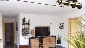 Una sala de estar con televisor, mueble de madera y una planta.
