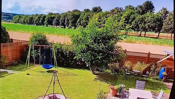 Un patio trasero con un tobogán, una mesa y sillas, y vistas a un campo y árboles.