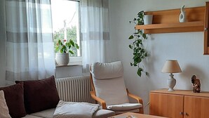 Una sala moderna con un conjunto de sofá, una mesa de centro, un radiador, una ventana con cortinas, una planta colgante y una lámpara.