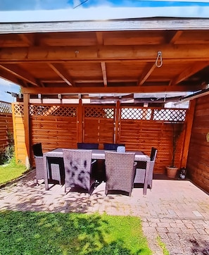 Une terrasse couverte avec une table et des chaises, une clôture en bois et une plante en pot.