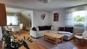 Una sala de estar con sofá, mesa de centro y sillas, un comedor con mesa y sillas, y una escalera que lleva a otra habitación.