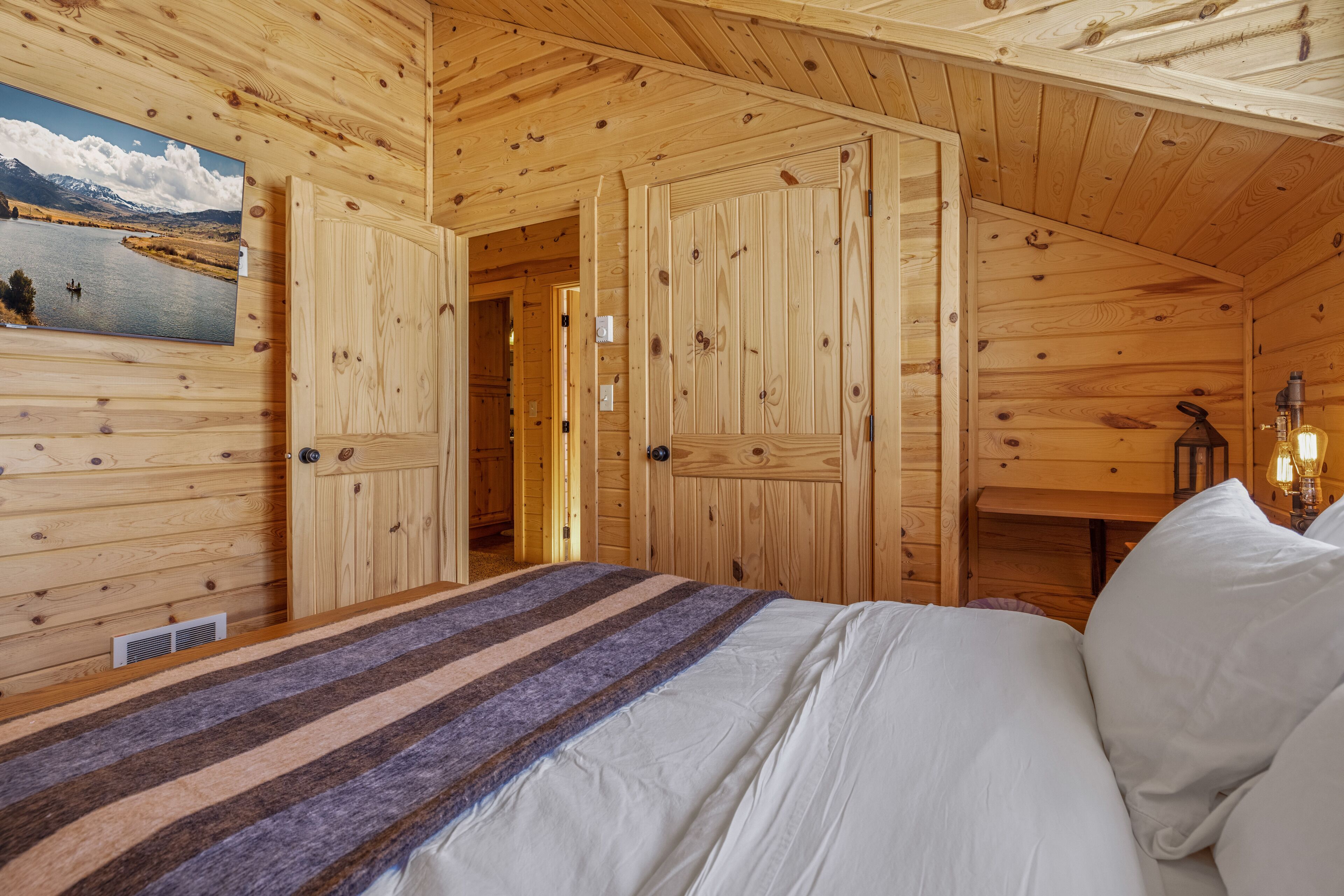 Camera da letto in una baita di legno, con un letto, un quadro che raffigura un lago e una porta in legno.