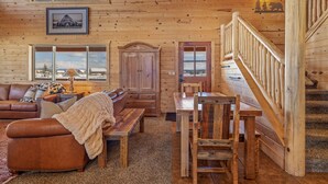 Interior de una cabaña de madera con sala de estar, comedor y escalera.