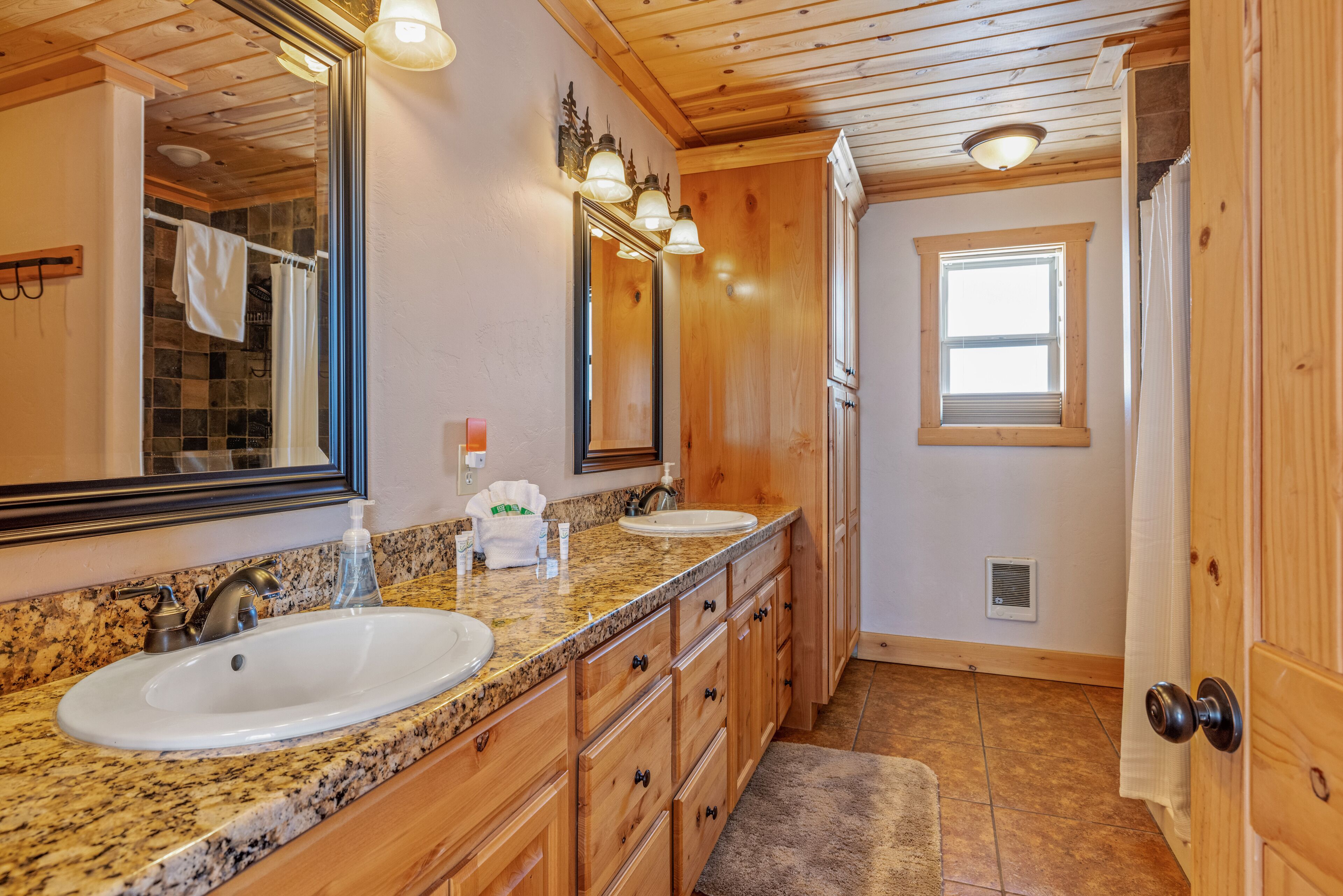 A bathroom with two sinks, wooden cabinets, a large mirror, and a window.