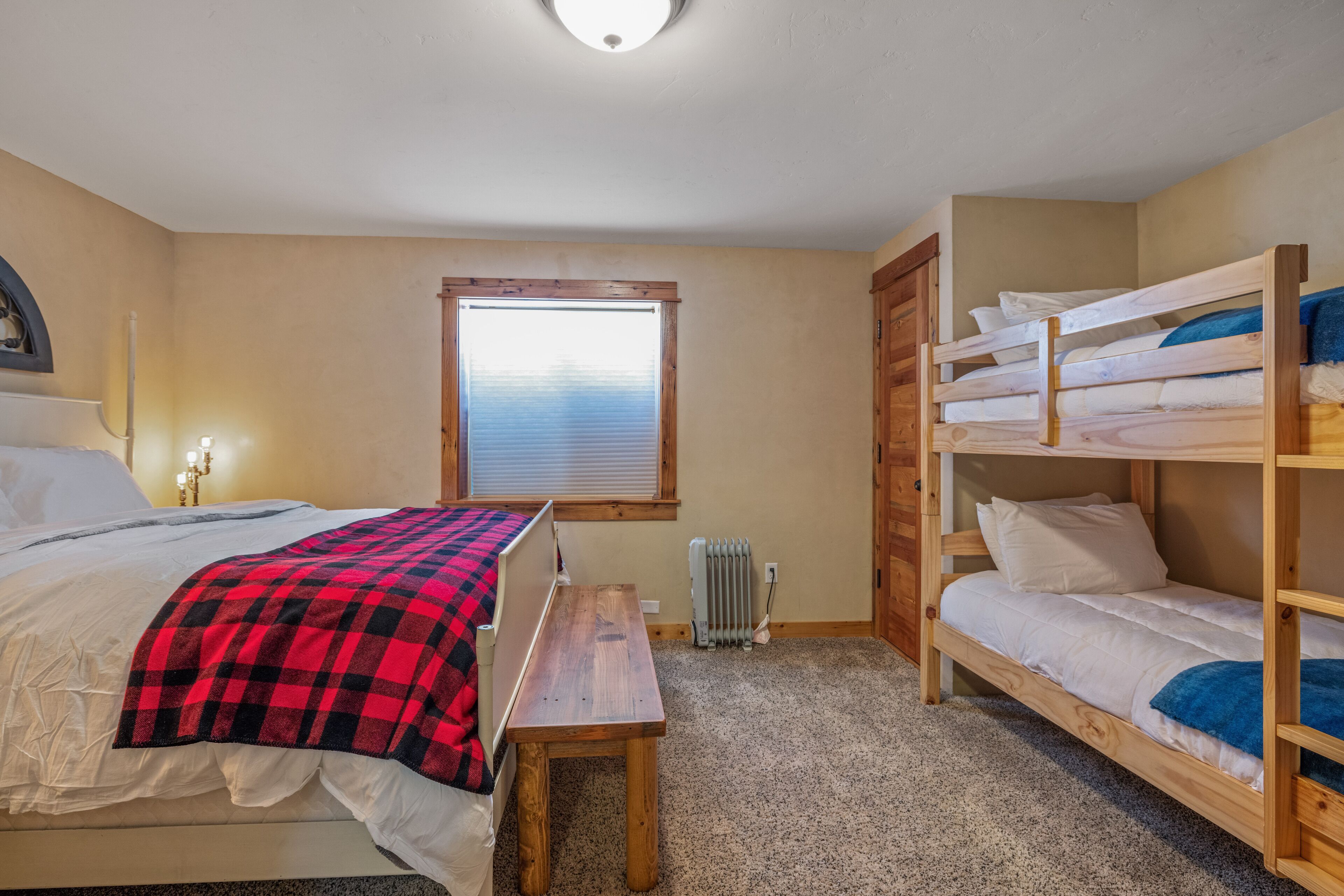 Un dormitorio con una cama, un banco, una ventana y una litera.