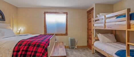 Un dormitorio con una cama, un banco, una ventana y una litera.