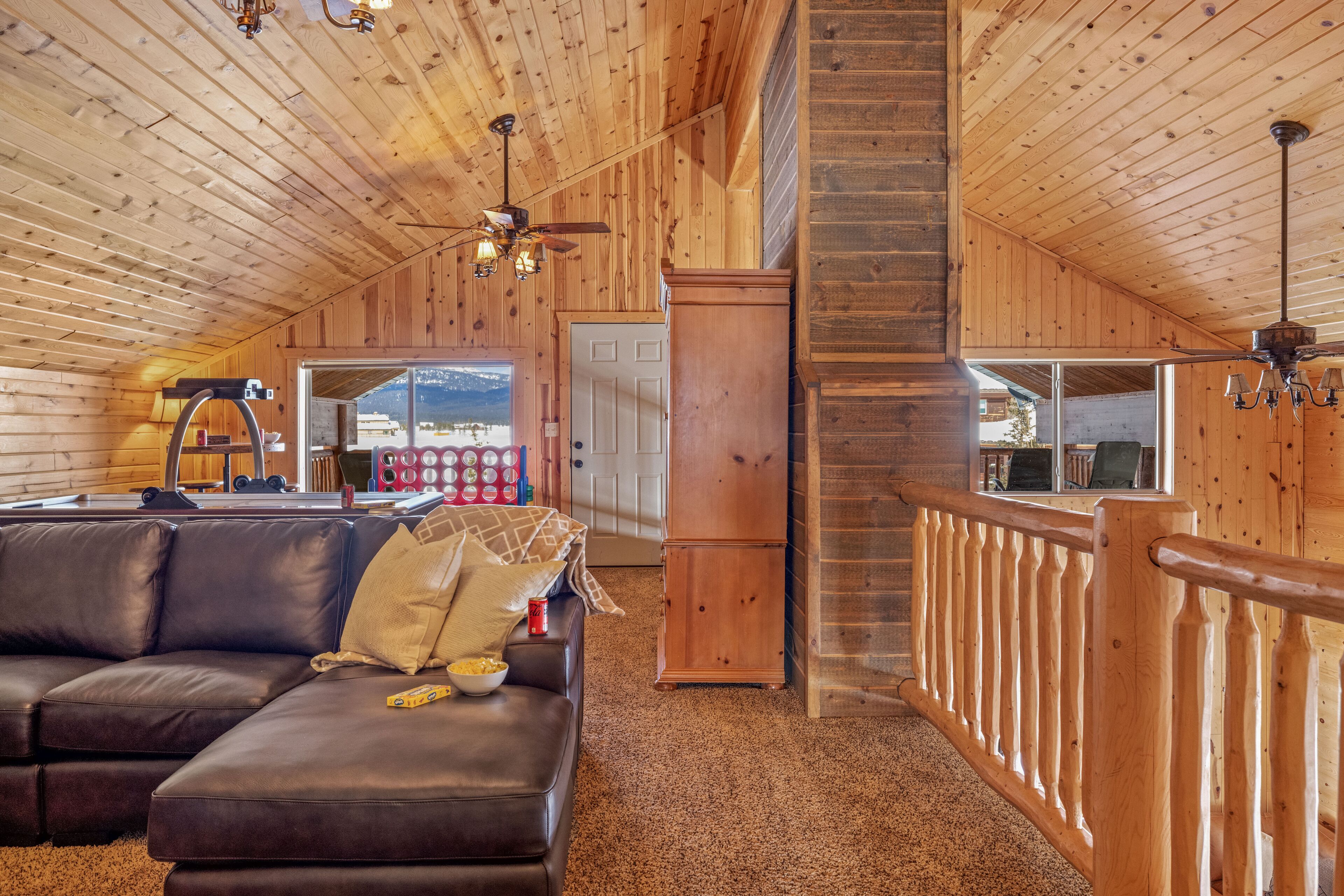 A cozy wooden interior with a leather sofa, a wooden cabinet, and a staircase leading to an upper level.
