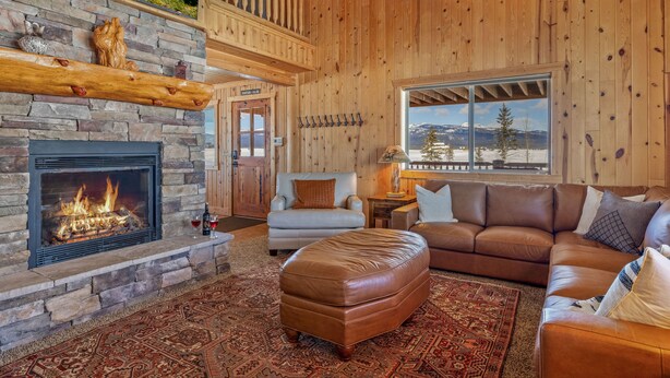 Una sala de estar acogedora con chimenea de piedra, muebles de cuero y vistas a un paisaje montañoso nevado.