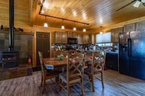 A wooden interior with a dining table, chairs, a kitchen with cabinets, a microwave, and a refrigerator. - Deer View (Island Park)
