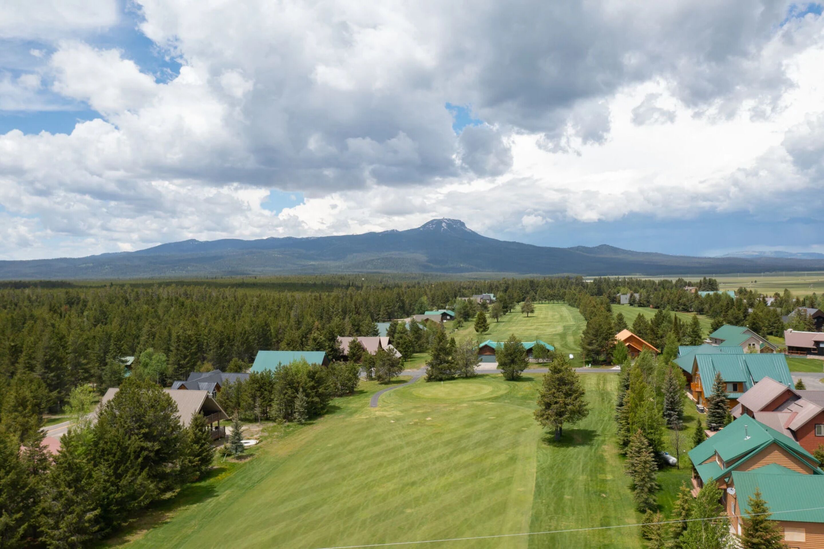 A residential area with houses, a green field, and a mountain in the background.