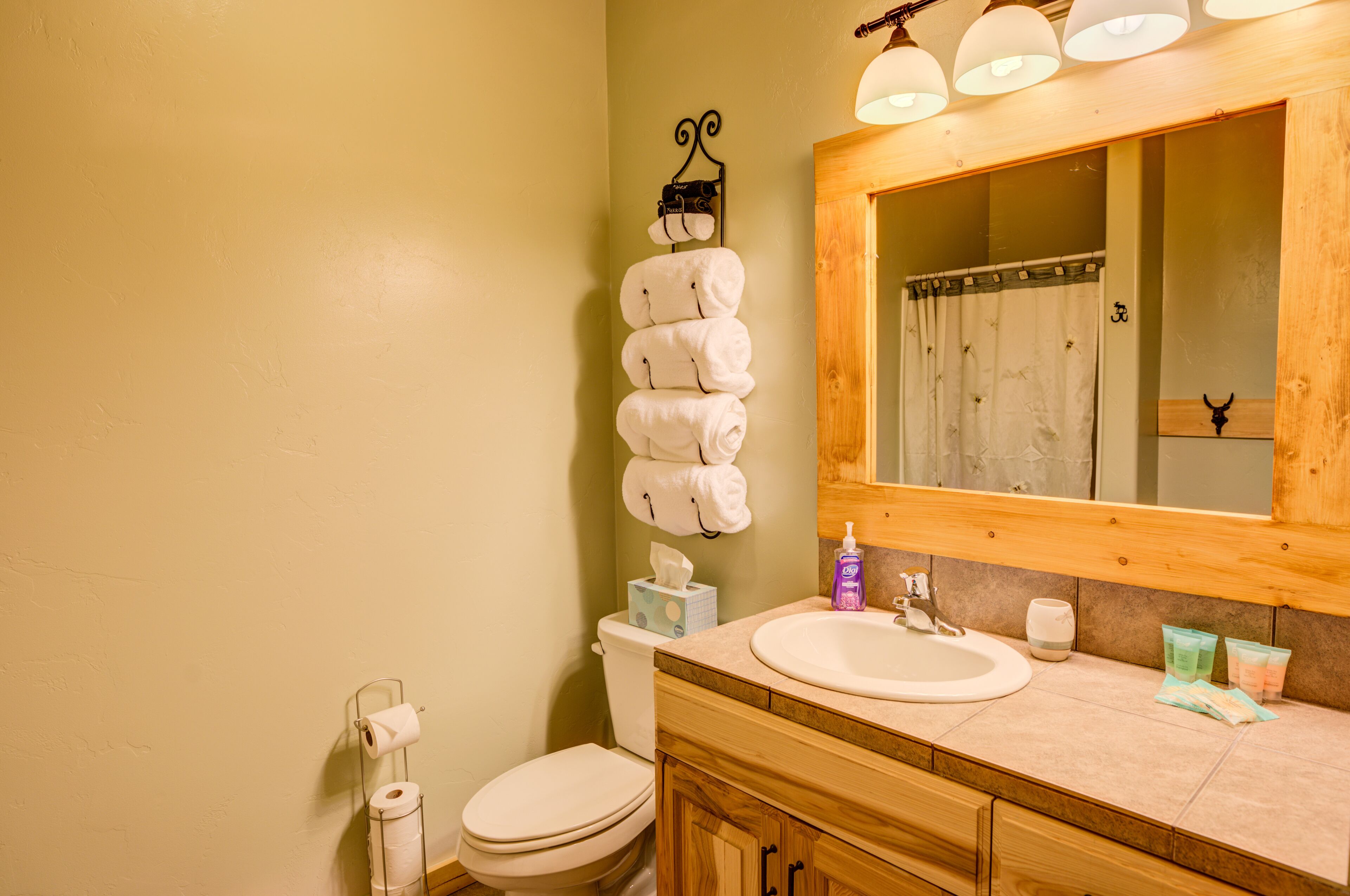 A bathroom with a wooden vanity, a sink, and a mirror. There are towels hanging on a rack, a toilet, and a roll of toilet paper.