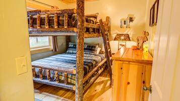 A bunk bed with a wooden ladder, a small wooden desk, and a wall-mounted lamp.