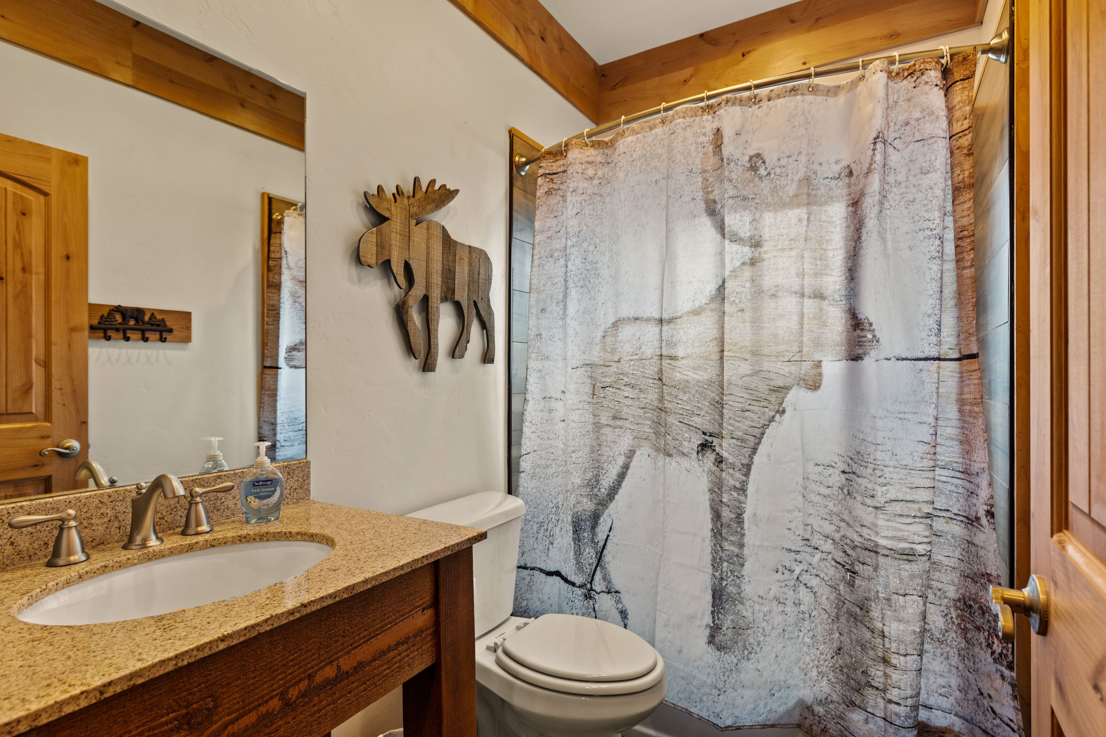 Ein Badezimmer mit Marmorwaschtisch, einem Holz-Waschtischunterschrank, einer weißen Toilette und einer Duschvorhang mit Elch-Motiv.
