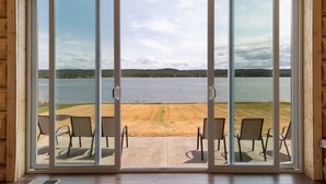 A room with a large sliding glass door leading to a patio with chairs and a view of a lake. - Stone Skipper Lodge (Island Park)