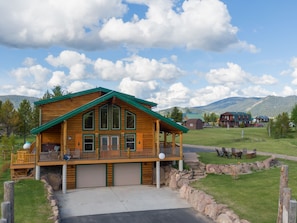 A log cabin with a large deck, garage doors, and a stone retaining wall. - Henrys Hawk (Island Park)