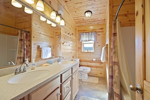 A wooden cabin bathroom with two sinks, a toilet, and a shower. - Henrys Hawk (Island Park)