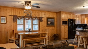 Un intérieur en bois comprenant une table à manger, des chaises, un canapé et un coin cuisine avec un réfrigérateur et une cuisinière.