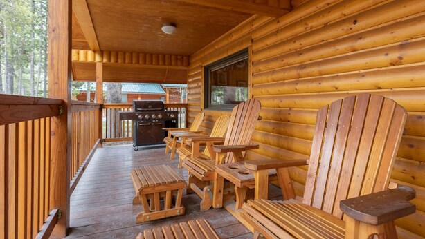 Une cabane en bois avec une véranda, des chaises et des tables en bois, ainsi qu’un barbecue.