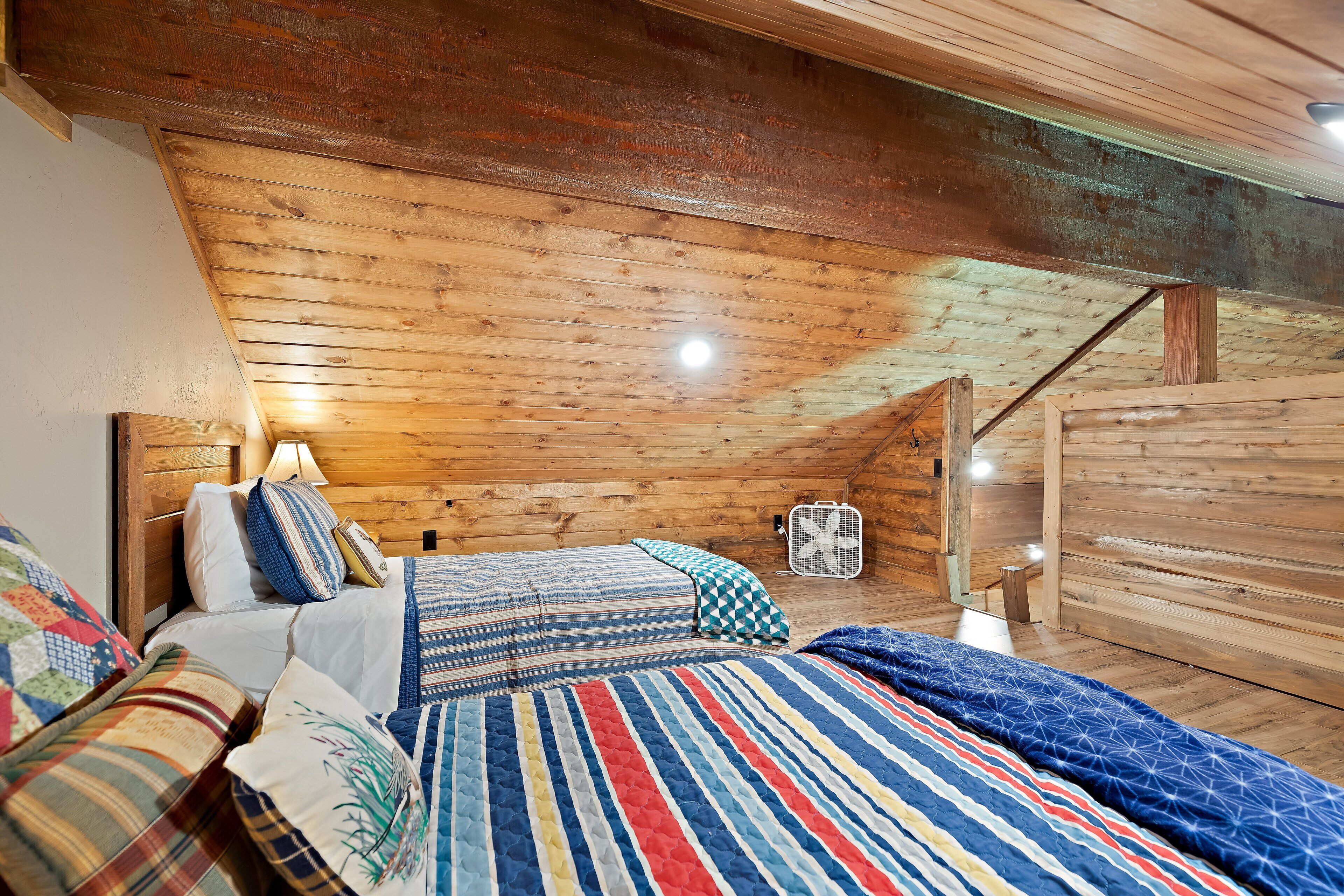 Un dormitorio acogedor en el ático, con vigas de madera, una cama con varios acolchados, un ventilador y una puerta de madera.