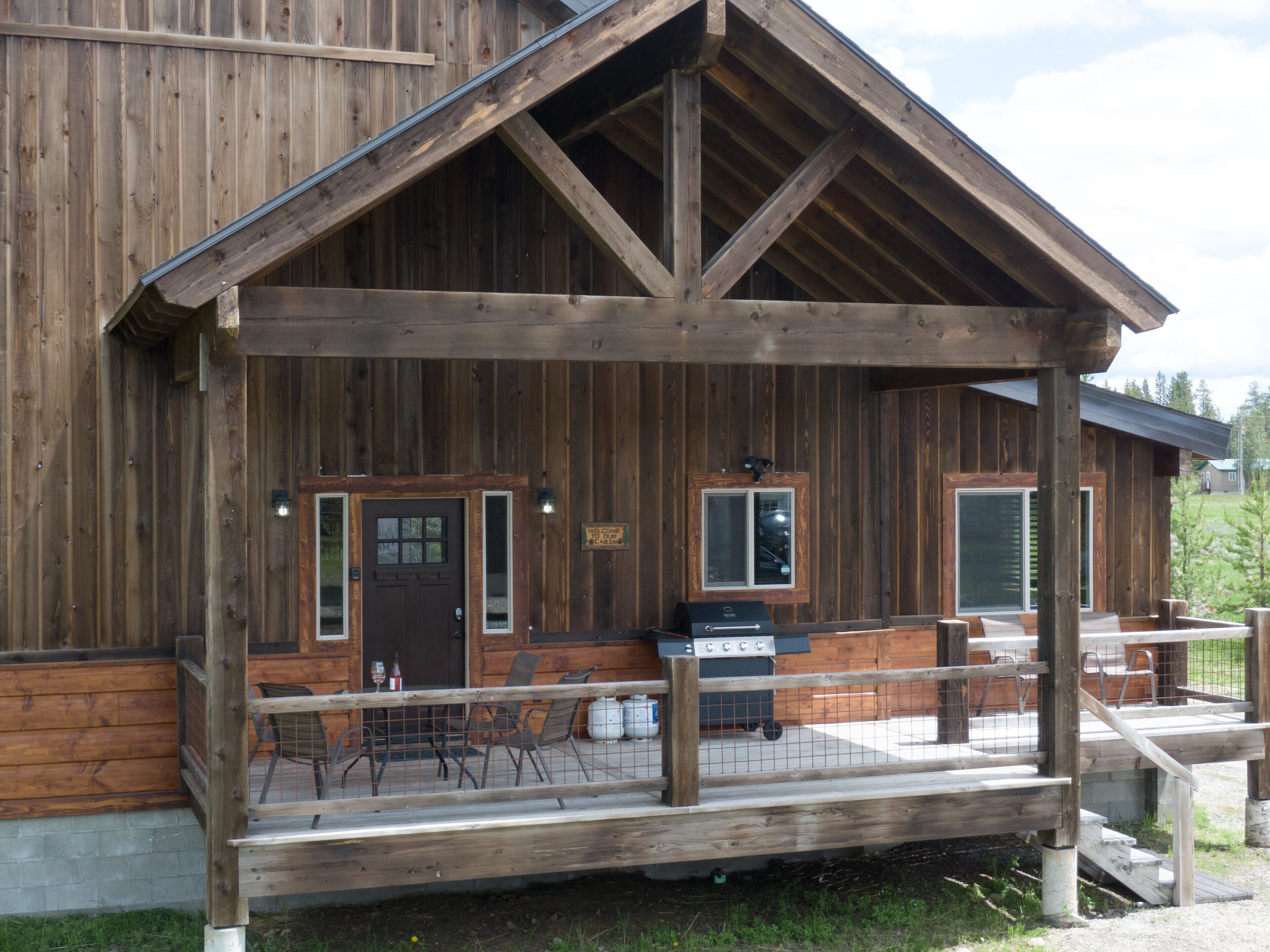 Une cabane en bois avec une véranda, un barbecue et une pancarte de bienvenue.