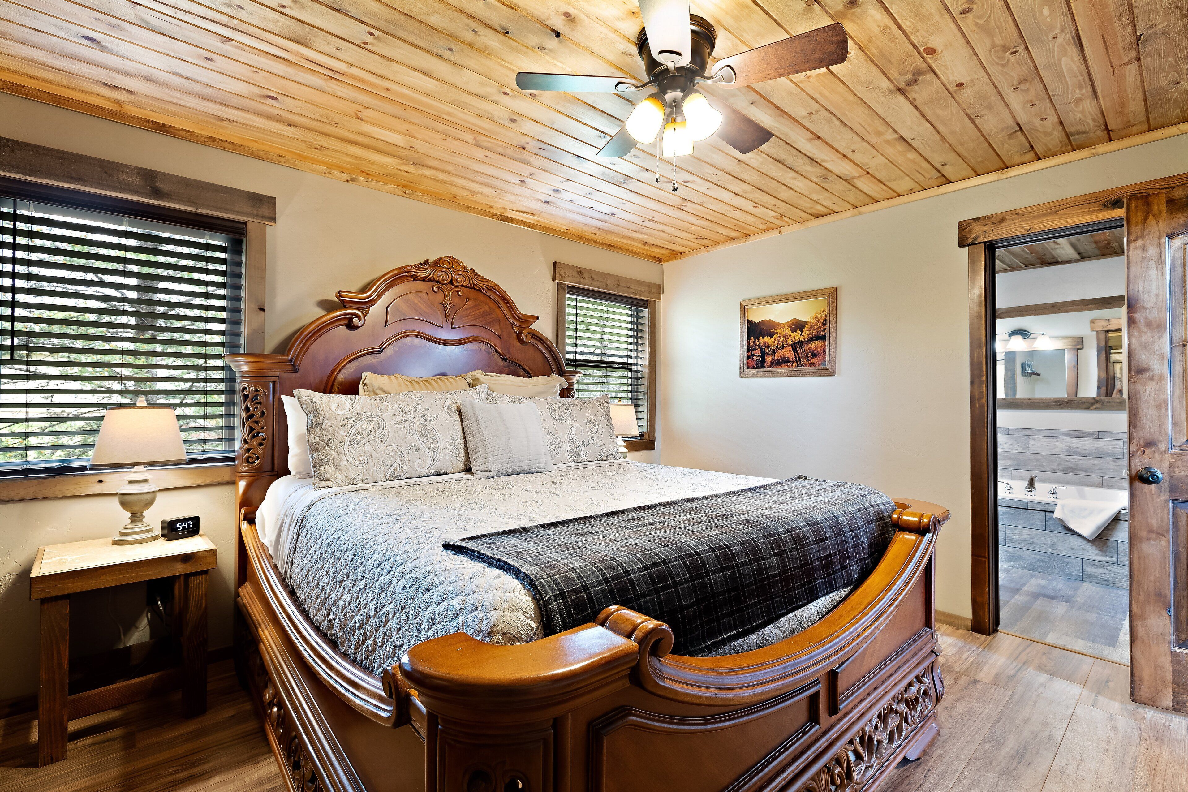 A wooden ceiling fan, a bed with a headboard, a nightstand, a window with blinds, and a painting on the wall.