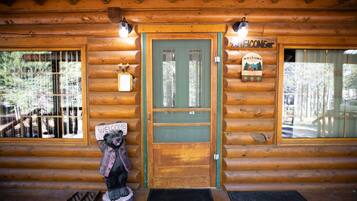 Une cabane en bois avec une porte verte, une statue d’ours tenant une pancarte et une enseigne « Bienvenue » au-dessus de la porte.