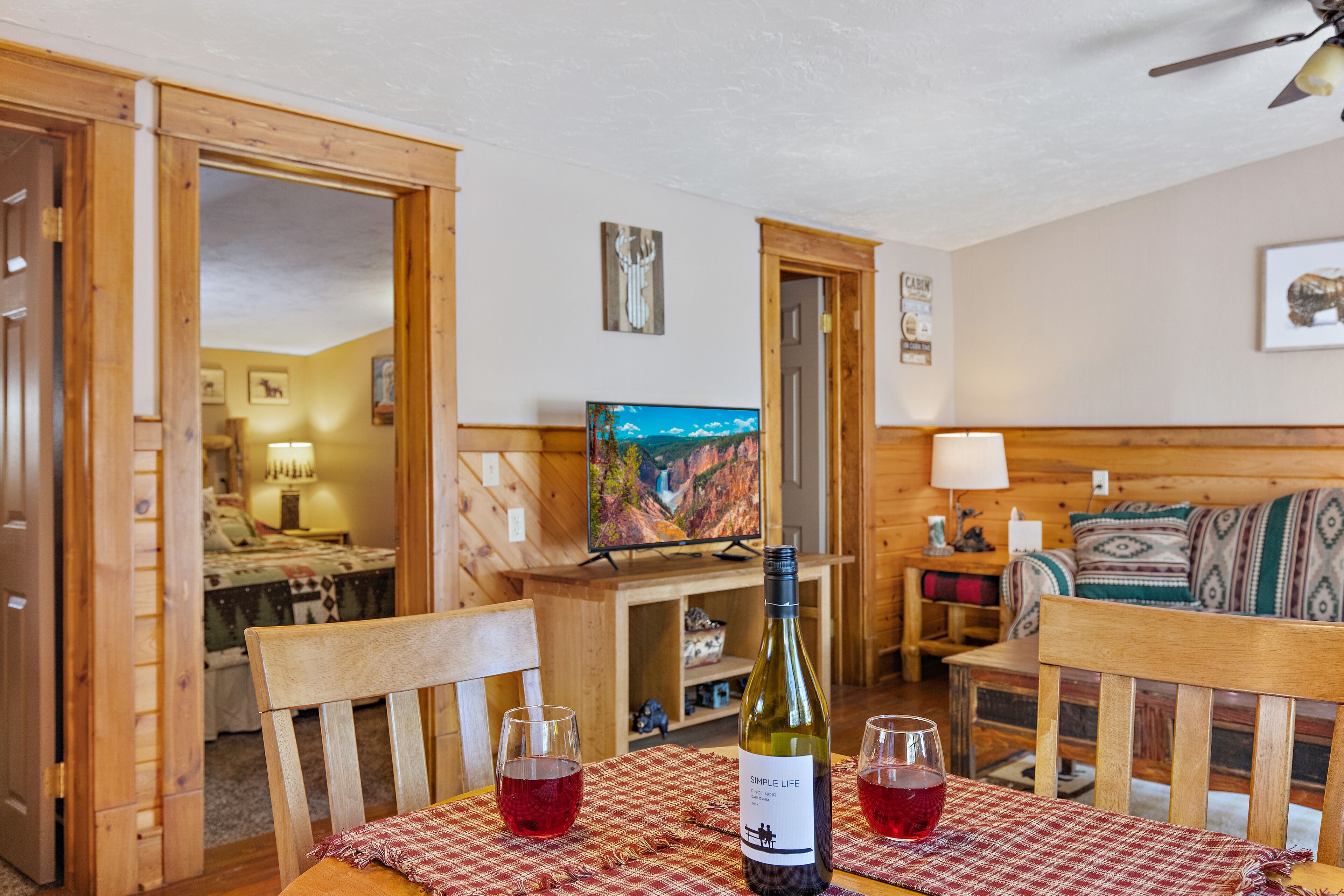 A wooden interior with a dining table, chairs, a bottle of wine, and glasses.