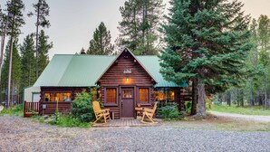 A log cabin with a green roof, two rocking chairs in front, and a gravel driveway. - Double Loop (Island Park)