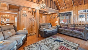 A rustic cabin interior with a wooden ceiling, a fireplace, a sofa, a recliner, and a rug with animal prints. - Double Loop (Island Park)