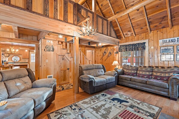 A rustic cabin interior with a wooden ceiling, a fireplace, a sofa, a recliner, and a rug with animal prints. - Double Loop (Island Park)