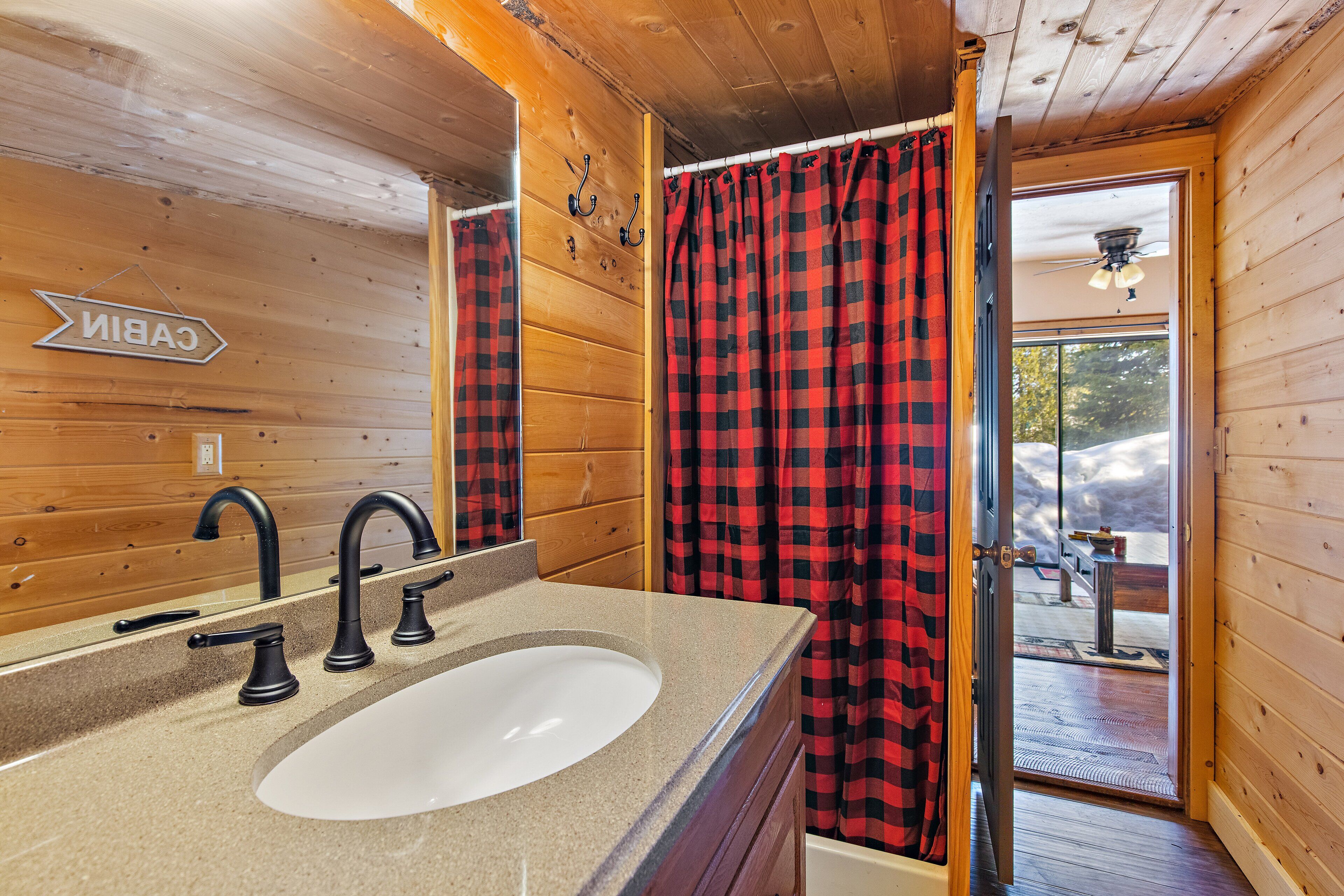 Un baño con detalles de madera, un lavamanos con espejo y una cortina a cuadros roja y negra.