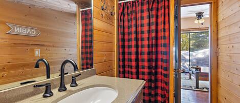 Un baño con detalles de madera, un lavamanos con espejo y una cortina a cuadros roja y negra.