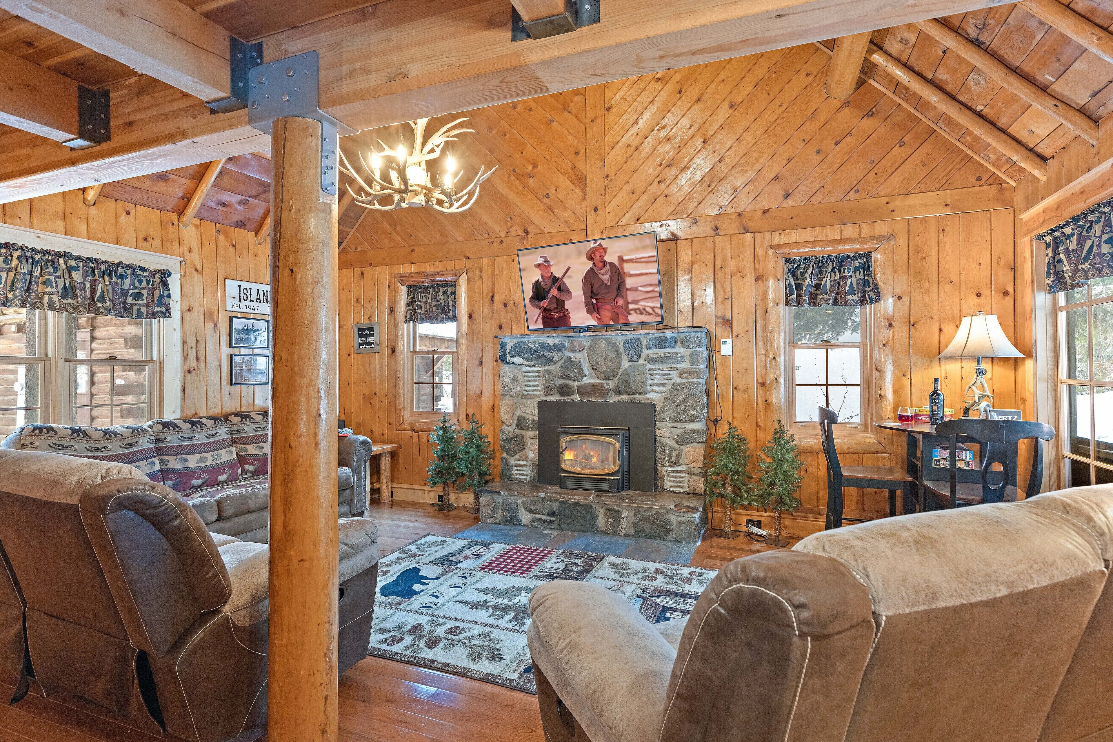 A cozy cabin interior with a stone fireplace, wooden walls, and a comfortable seating area.