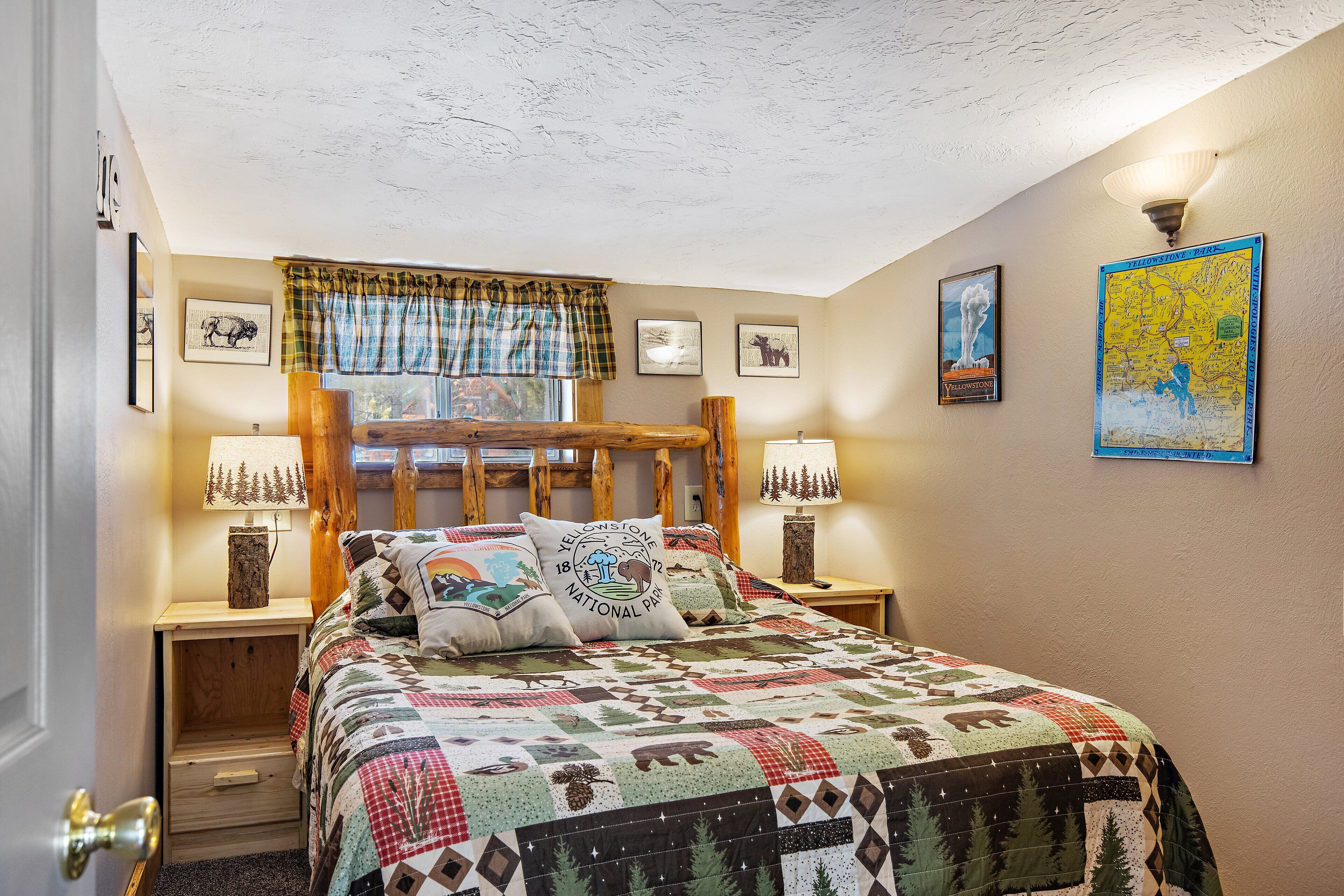 A bedroom with a wooden headboard, a quilted bedspread, two bedside lamps, and a window with plaid curtains.